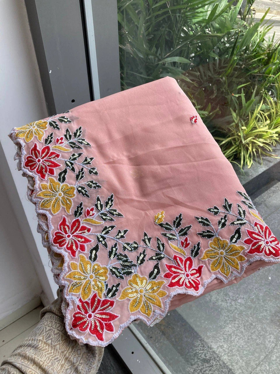 Pink fabric with floral embroidery draped over a surface near a window with plants.