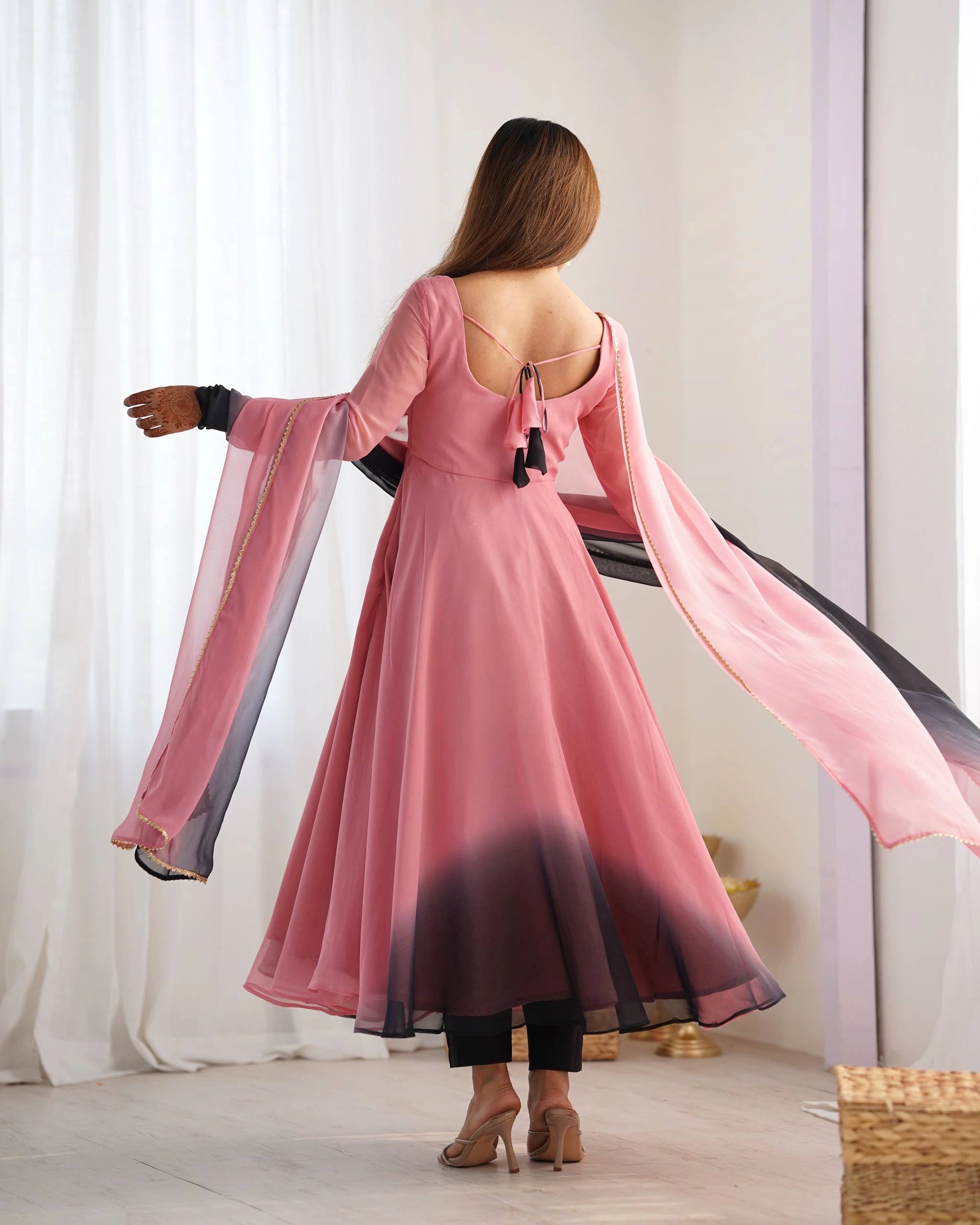 A rear view of a woman showing the deep back neckline of her pink dress, which features a delicate tie-up detail with black tassels.