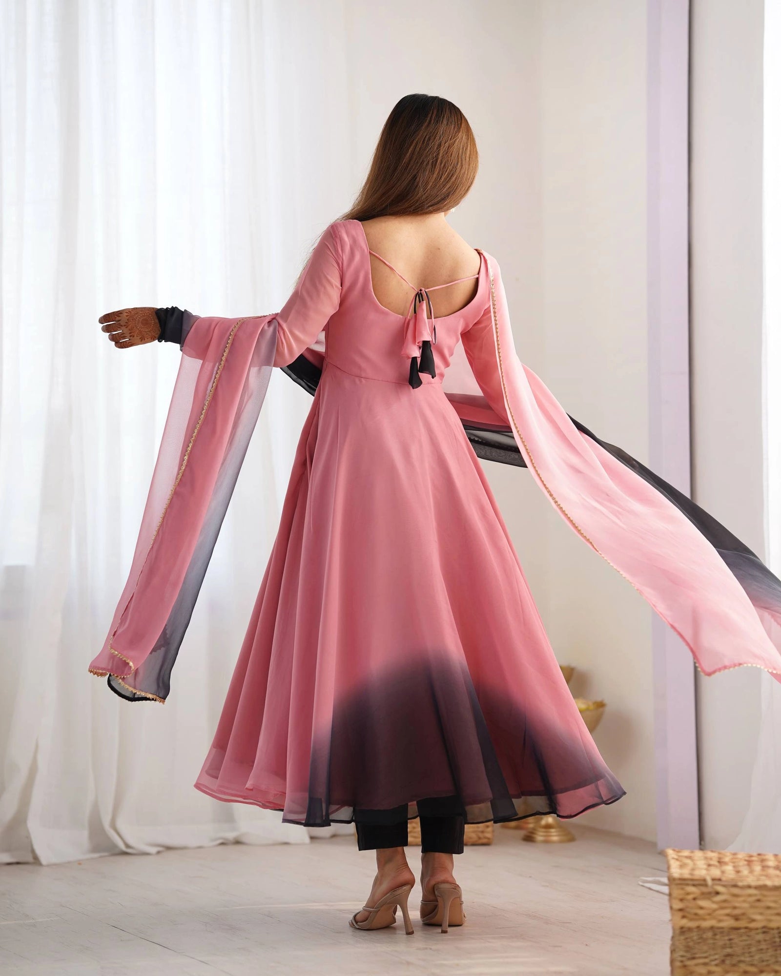 A rear view of a woman showing the deep back neckline of her pink dress, which features a delicate tie-up detail with black tassels.