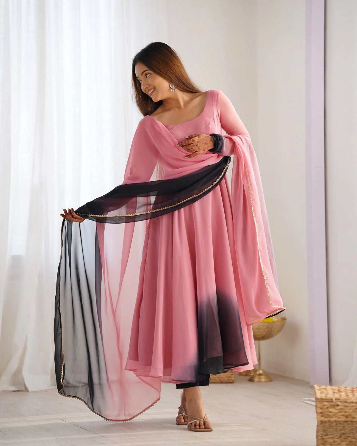 Woman in a pink traditional outfit with a black and pink dupatta against a white curtain background
