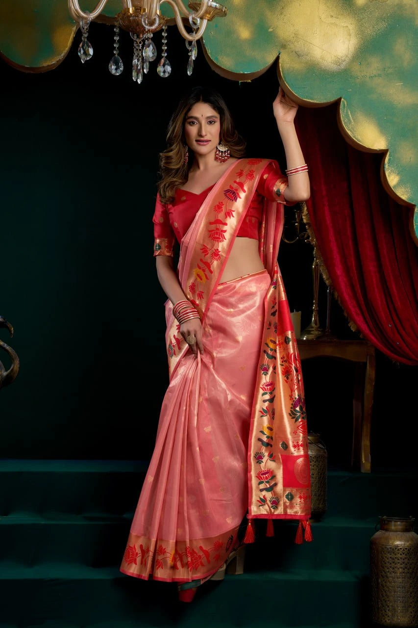Woman in a pink saree with red blouse standing in a decorated room.