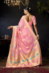 Woman in a pink saree with gold and blue patterns, standing against a dark background.