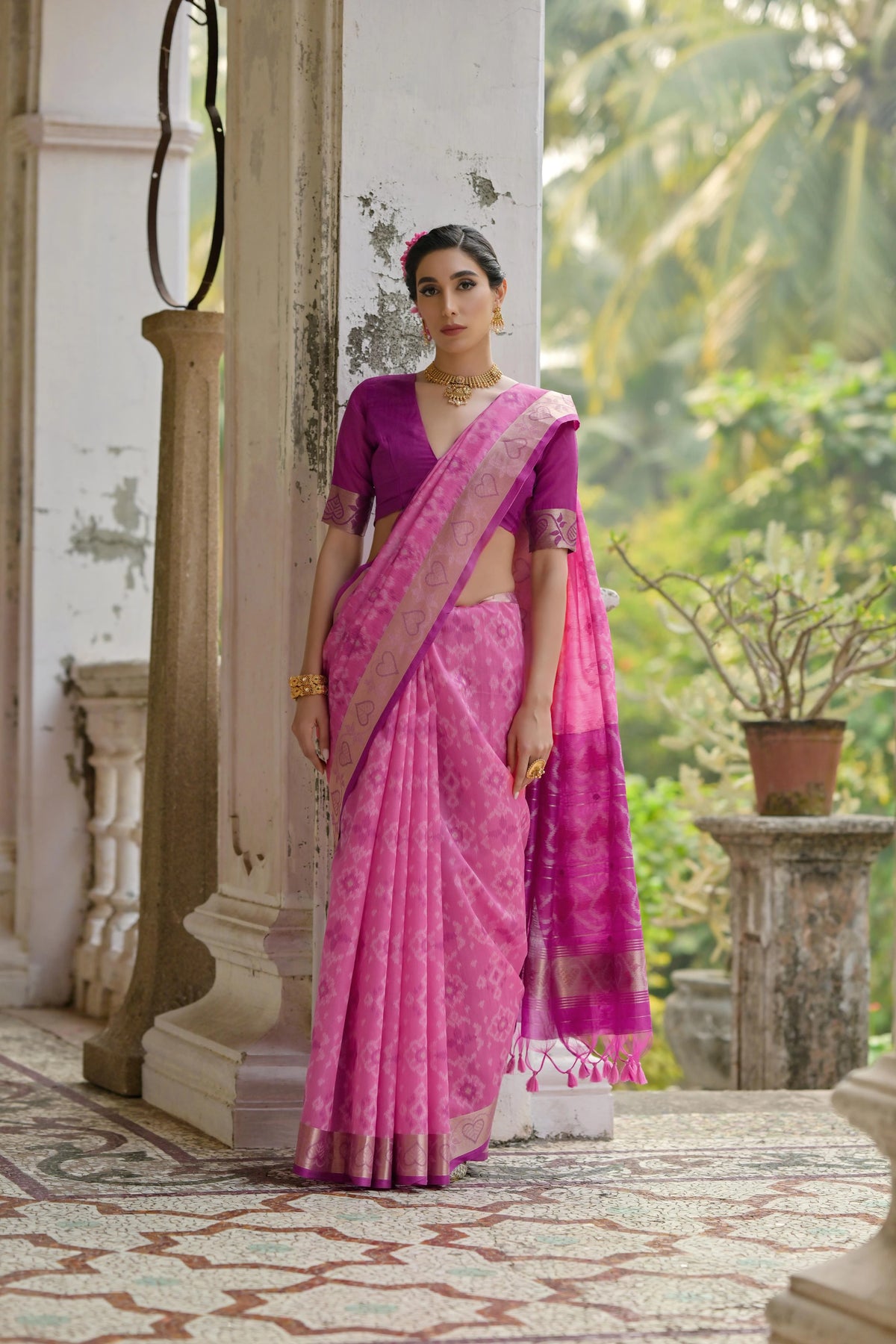 Woman in a pink saree standing outdoors with greenery in the background