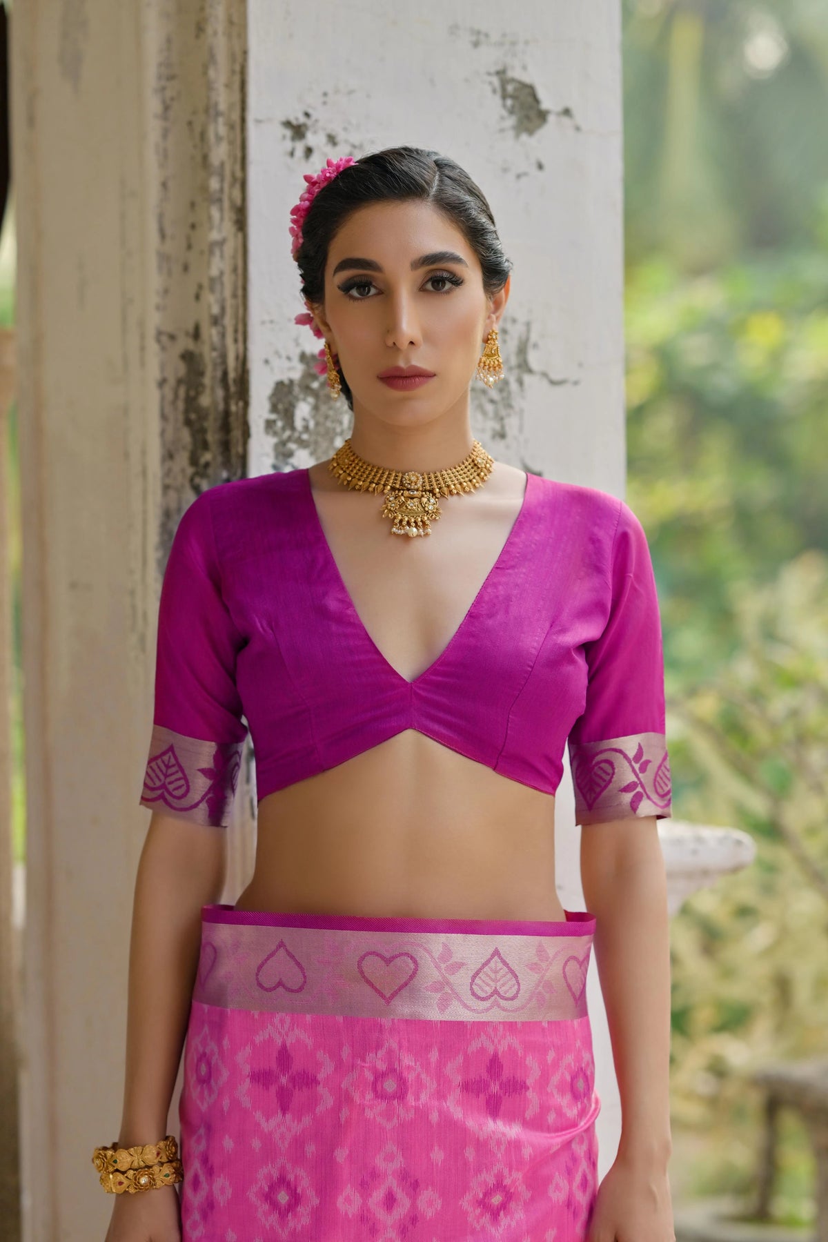 Woman wearing a pink traditional outfit with gold jewelry against a natural background