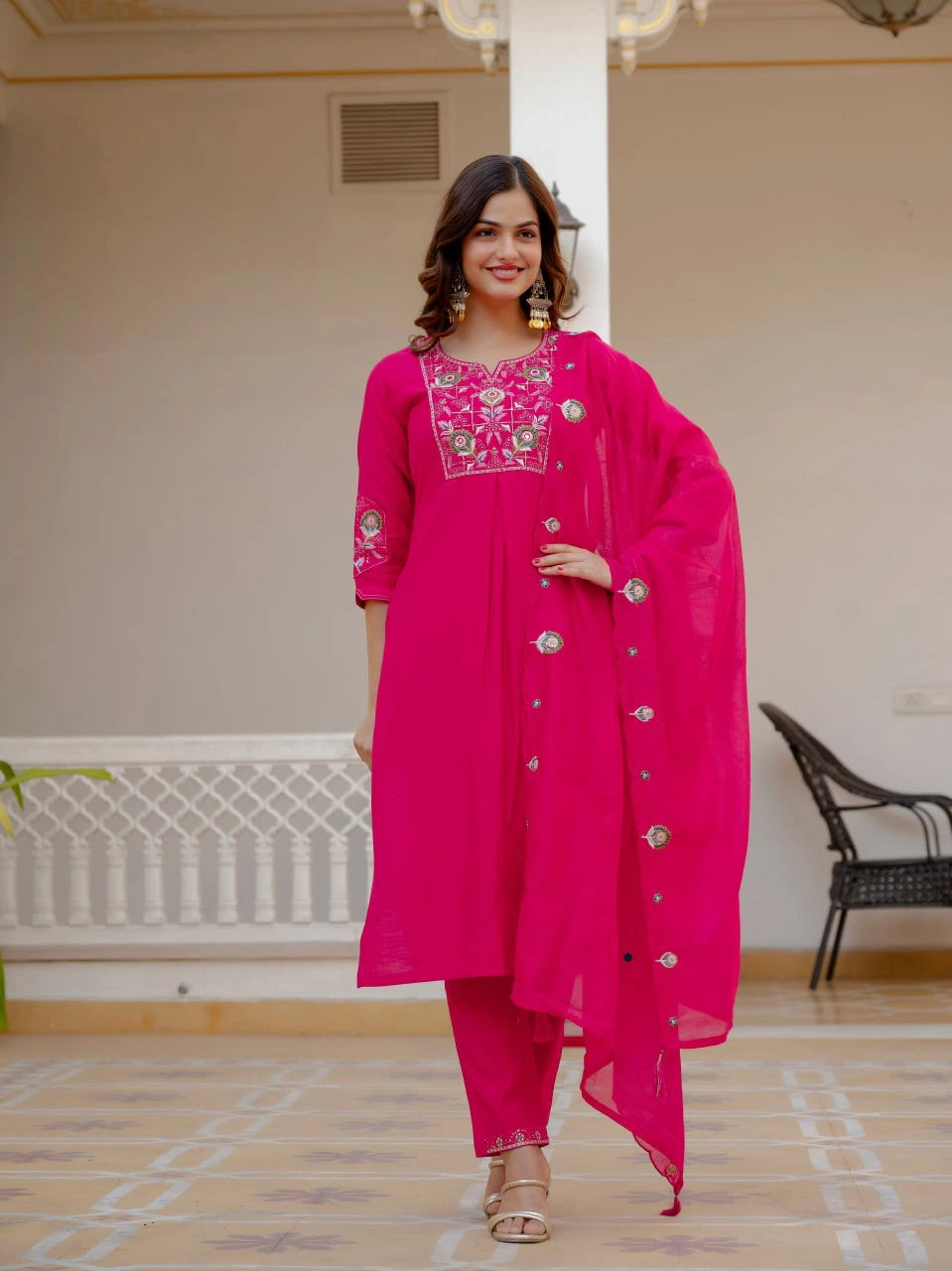 Woman wearing a bright pink traditional outfit with intricate designs indoors.