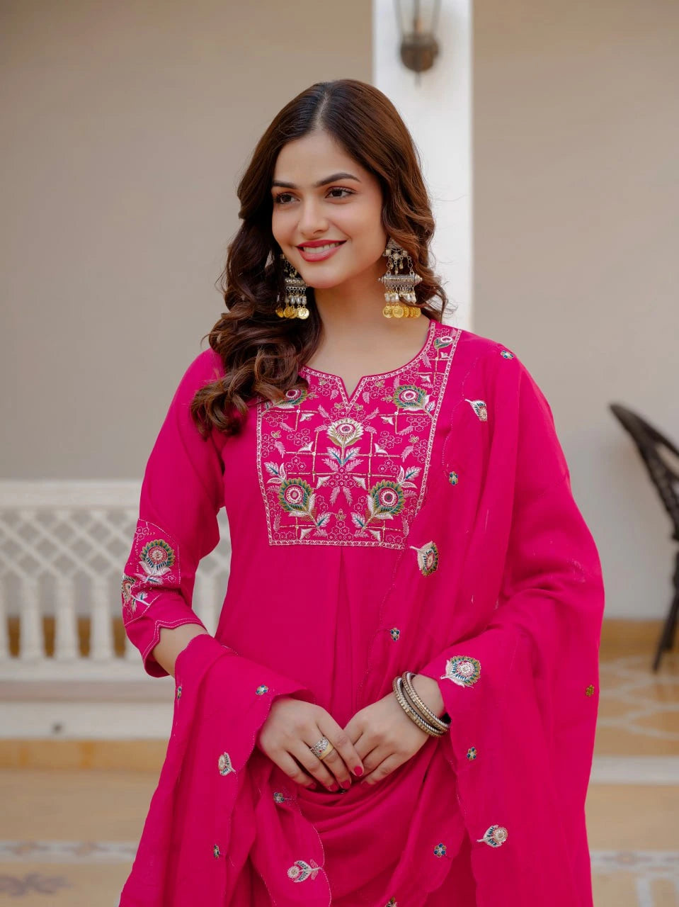 Woman wearing a bright pink traditional outfit with intricate embroidery indoors.