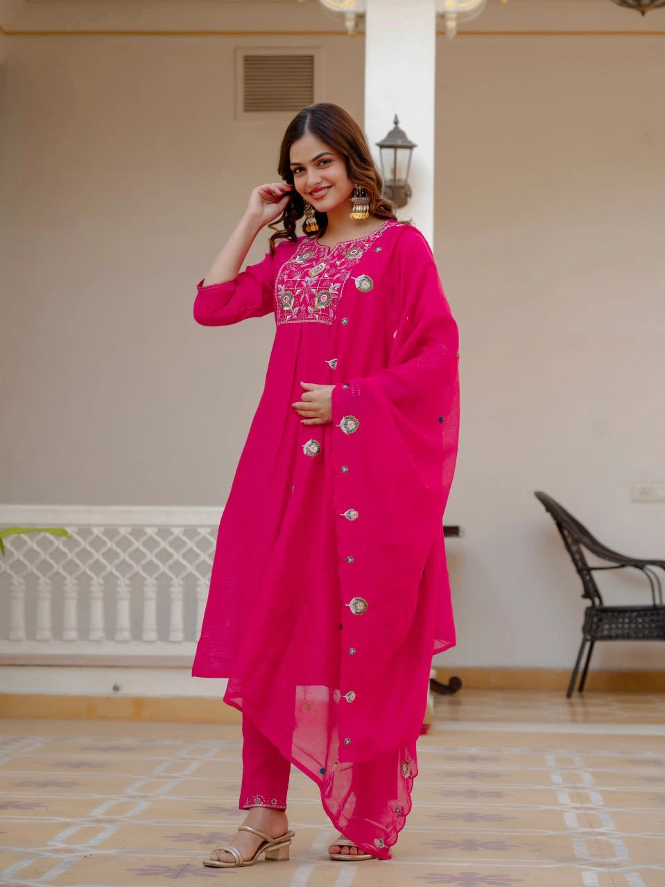Woman wearing a bright pink traditional outfit with intricate designs indoors.