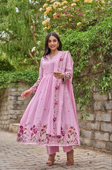 Woman in a pink embroidered outfit standing outdoors with greenery in the background