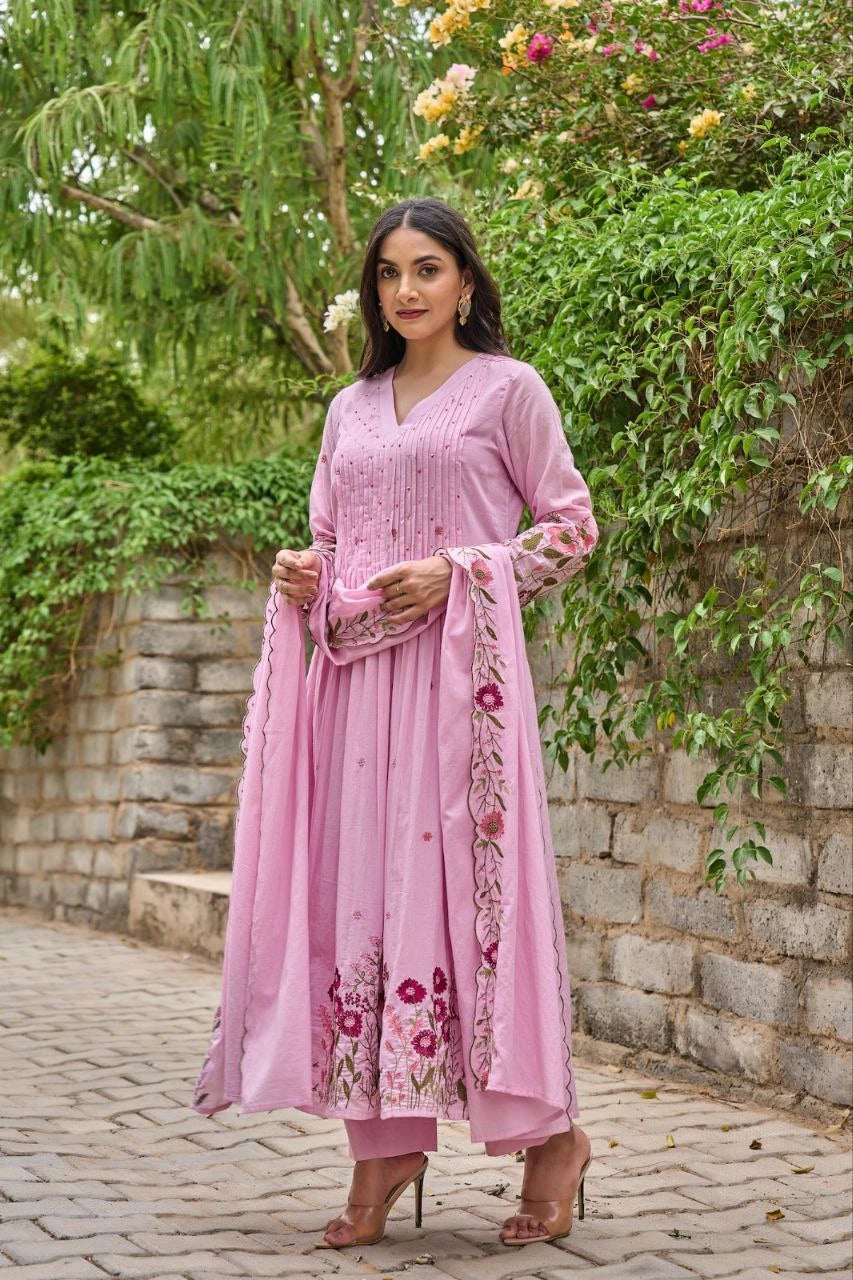 Woman in a pink traditional outfit standing outdoors with greenery in the background