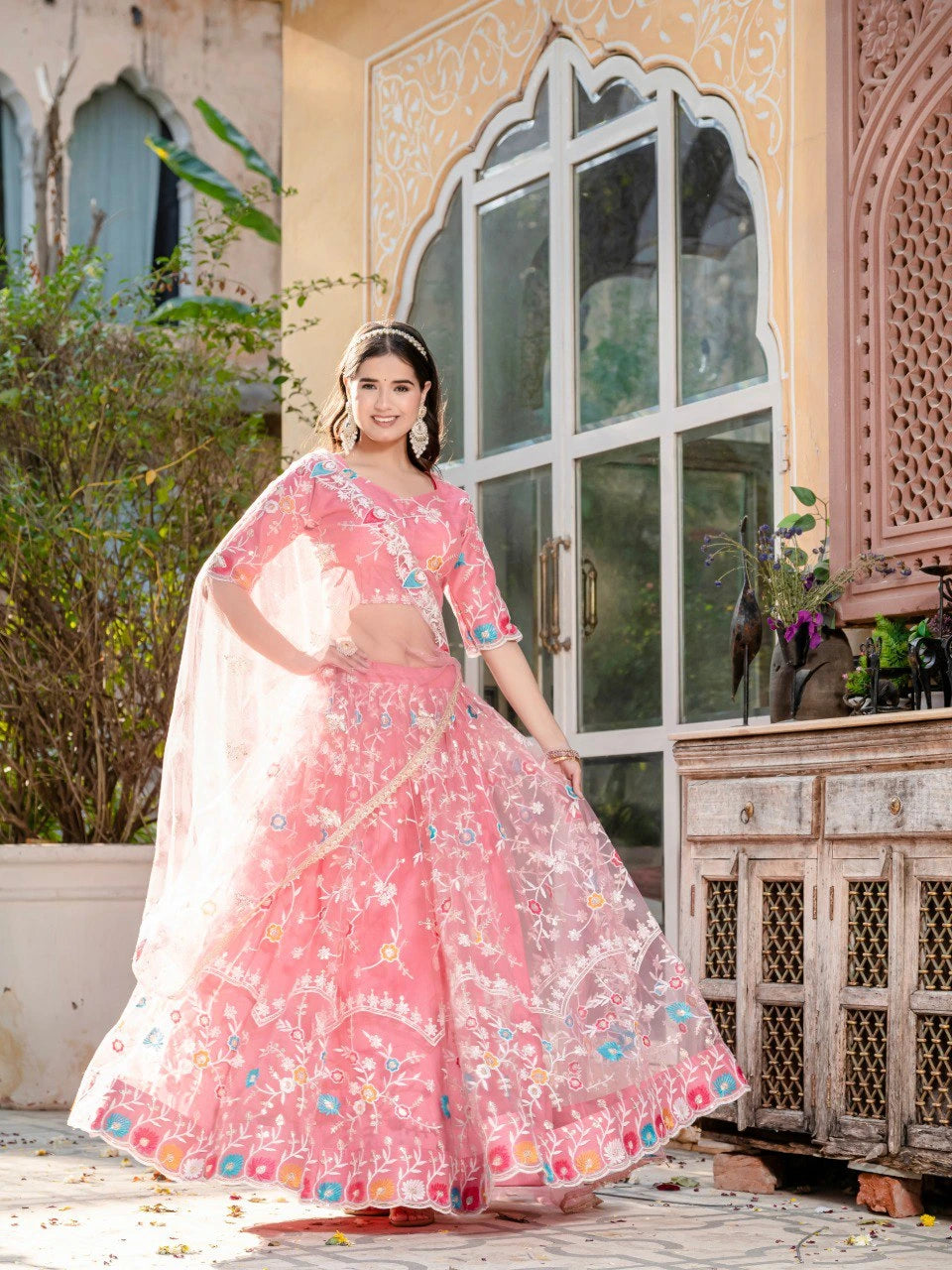 Woman in a pink traditional outfit standing in front of an ornate building.
