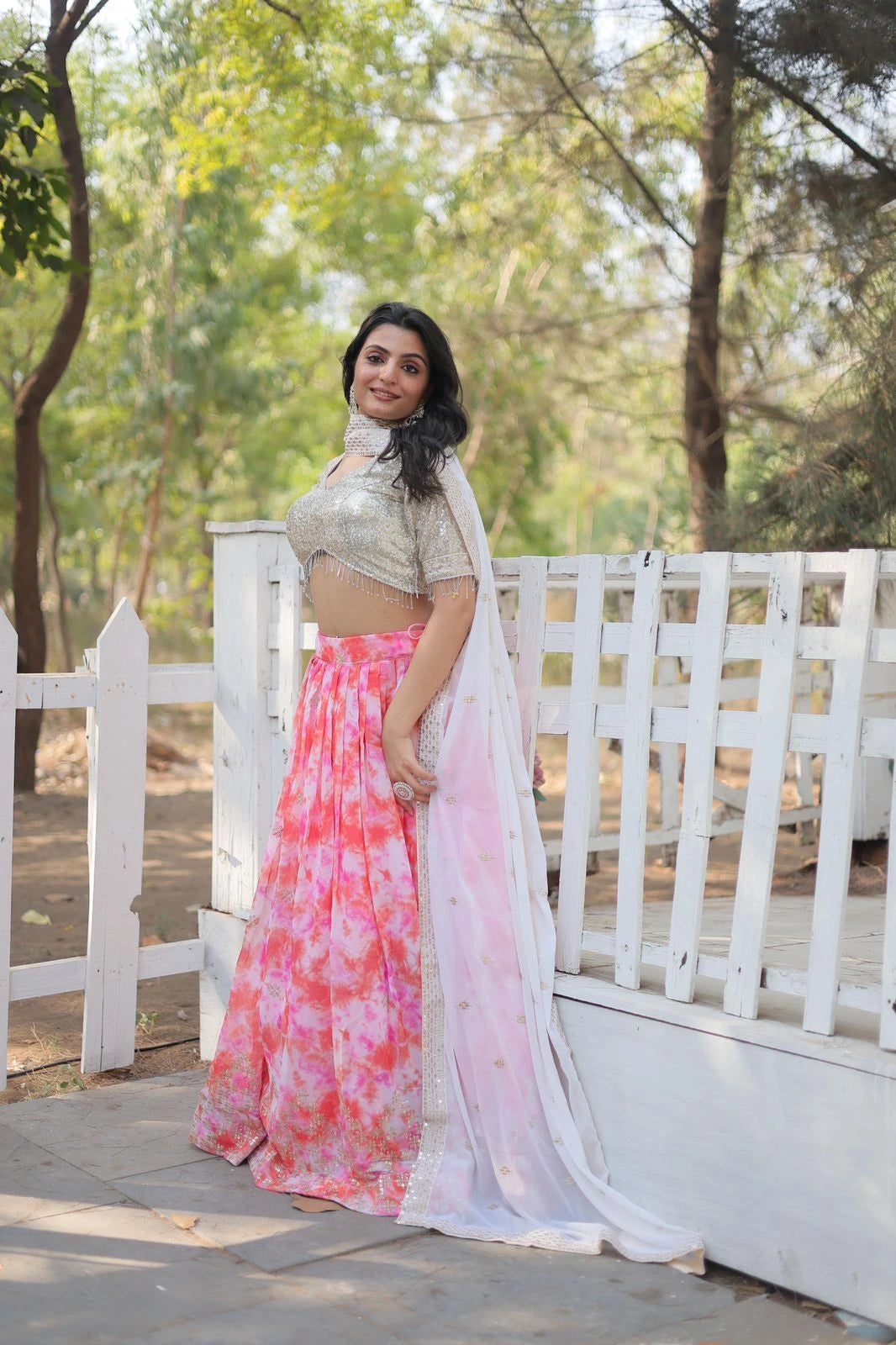 Woman in a floral outfit standing on a wooden platform with a white picket fence and greenery in the background