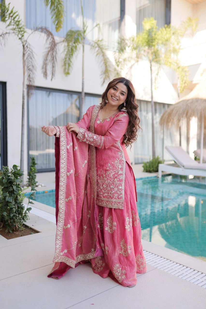 Woman in a pink traditional outfit standing by a pool with modern building and plants in the background
