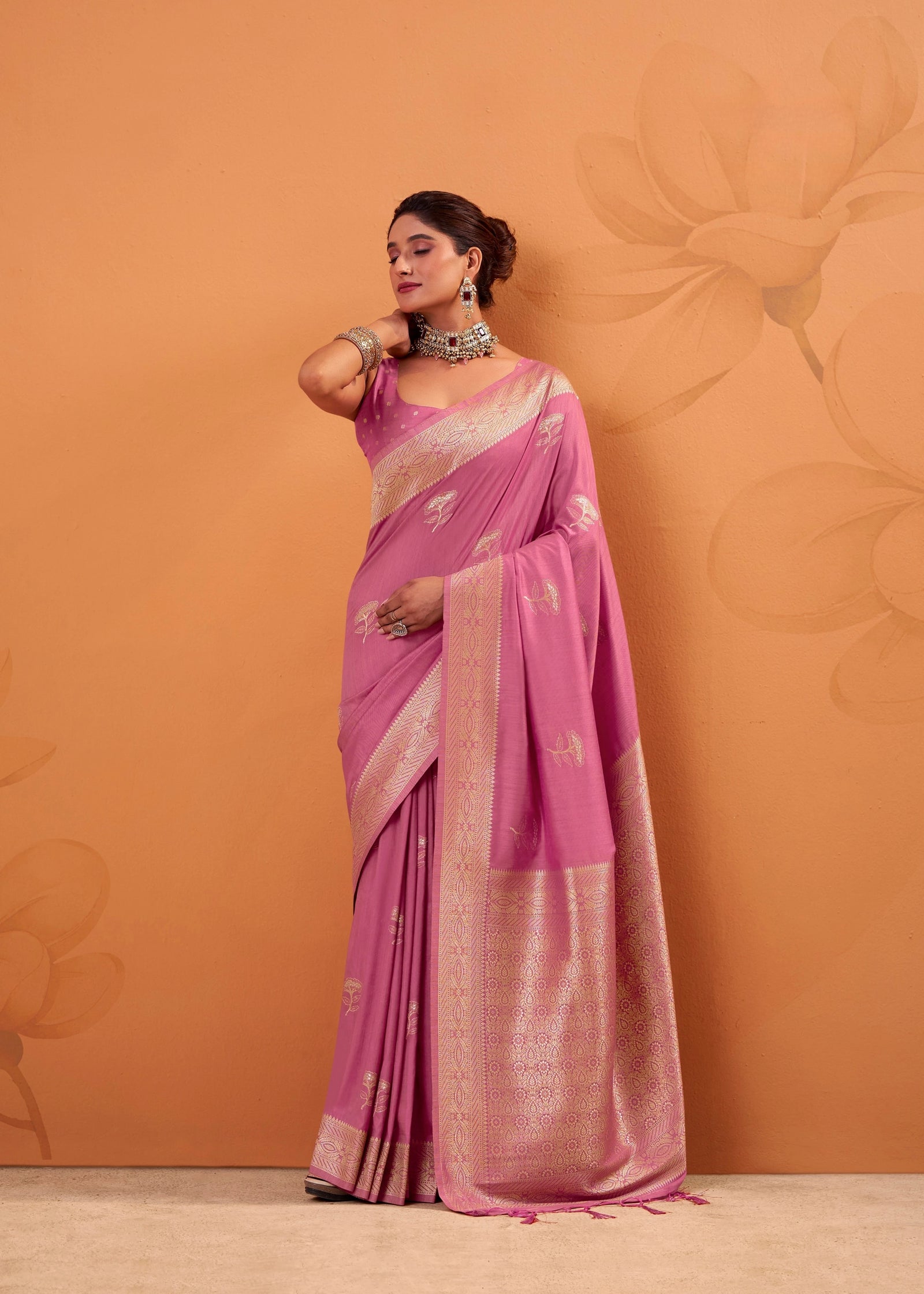 Woman wearing a pink saree with a floral pattern against an orange background