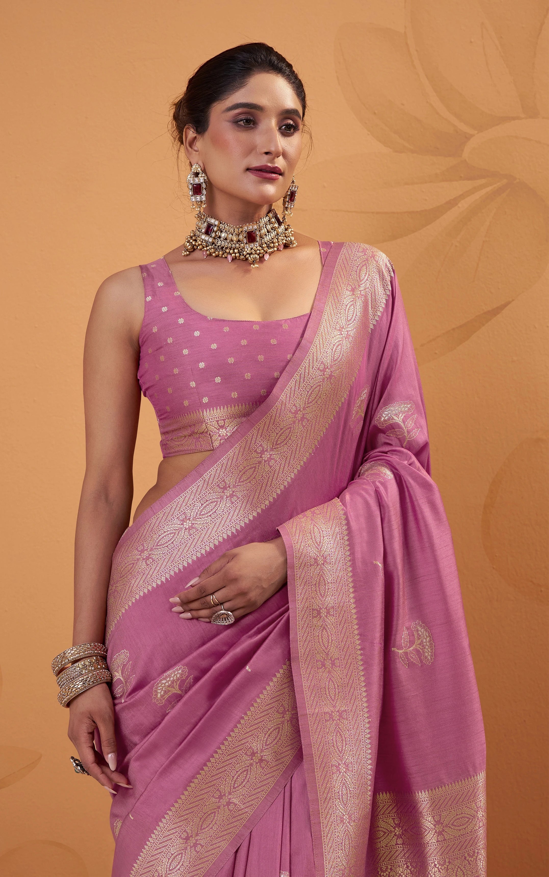 Woman wearing a pink saree with a gold border on an orange background