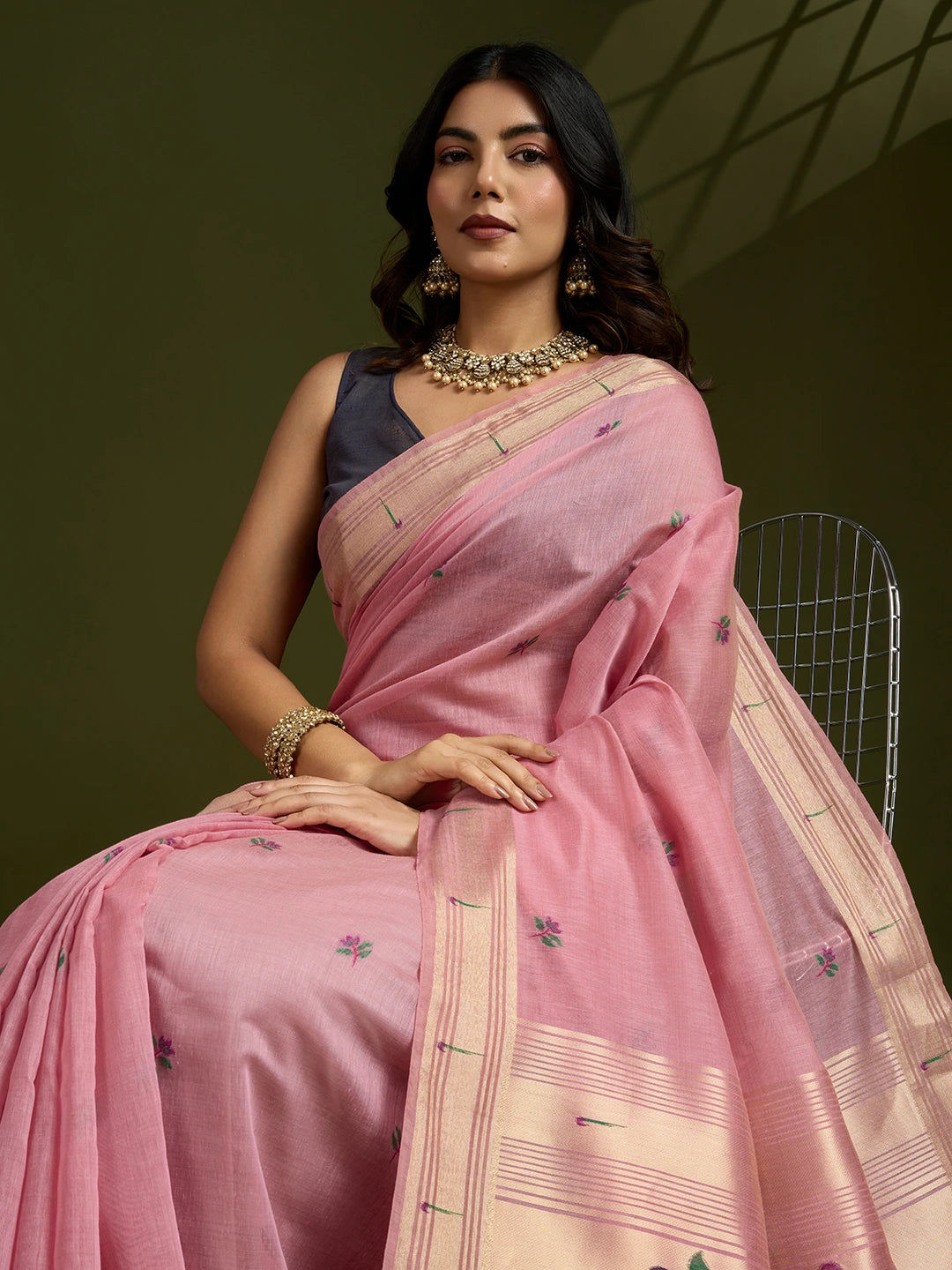 Woman wearing a pink saree with a dark blouse against a green background
