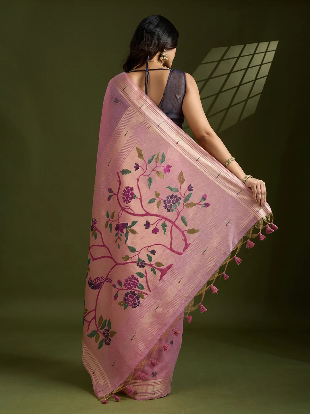 Woman holding a pink embroidered saree with floral patterns on a green background