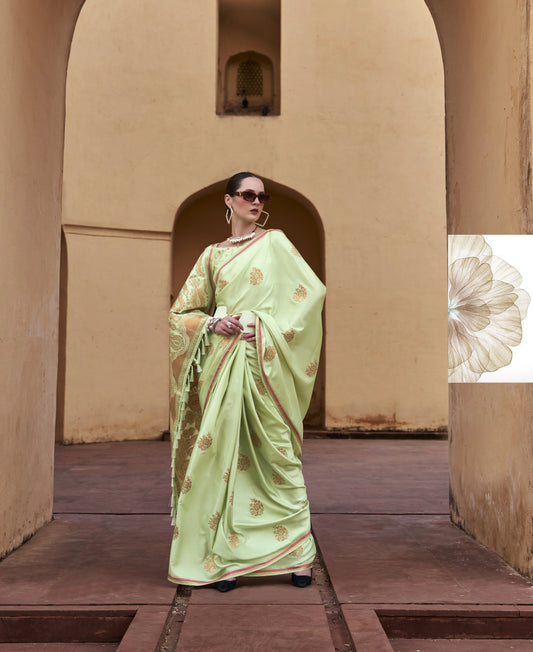 Woman in a light green saree standing in an archway with a beige wall and wooden floor.