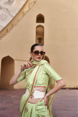 Woman in a light green saree with a beige wall and arches in the background