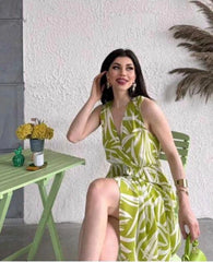 Woman in a green and white patterned dress sitting on a chair with a white wall and decorative elements in the background.
