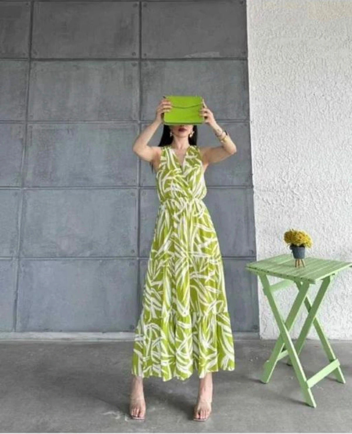 Woman in a green and white dress standing next to a small green table against a gray wall.