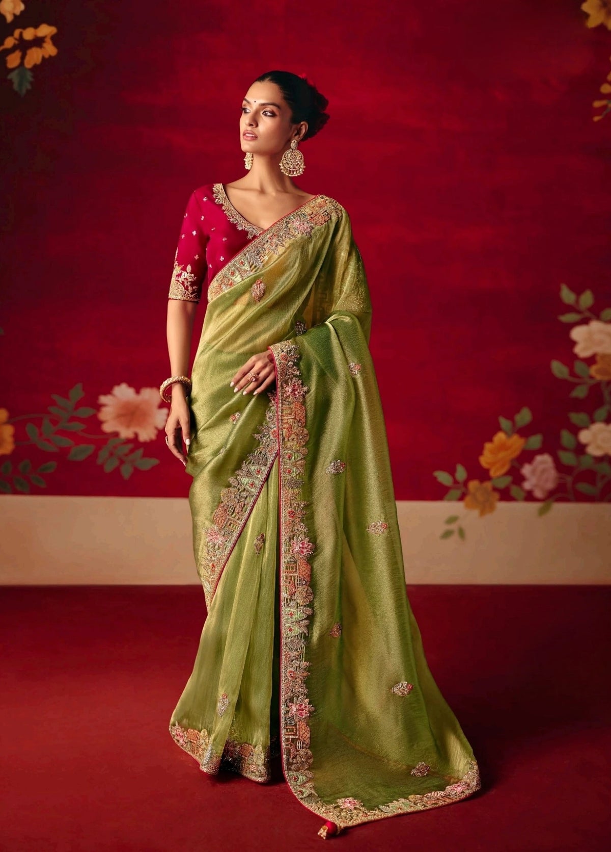 Woman wearing a green saree with a red blouse against a decorative red background