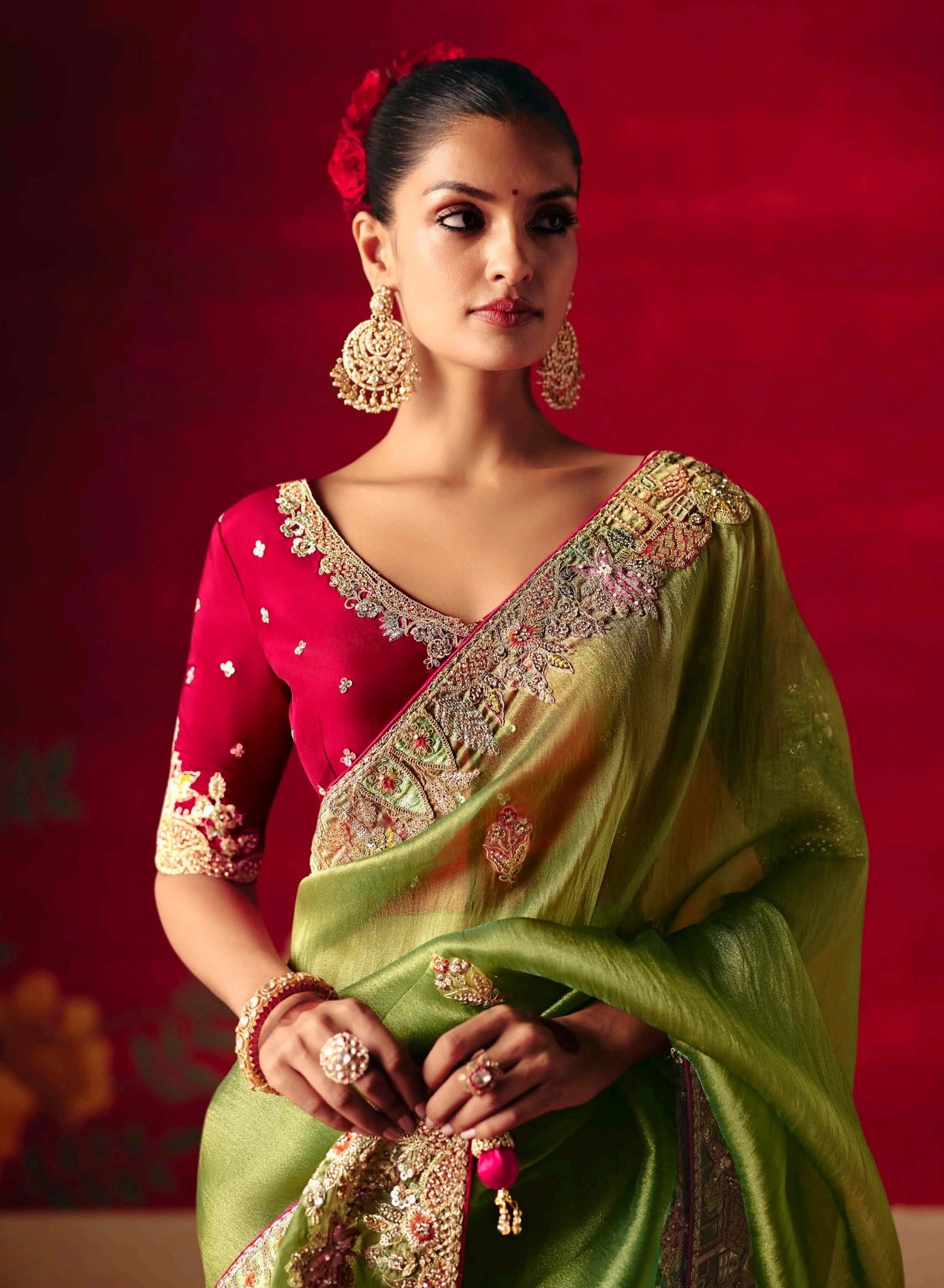 Woman wearing a green and red saree with intricate patterns against a red background