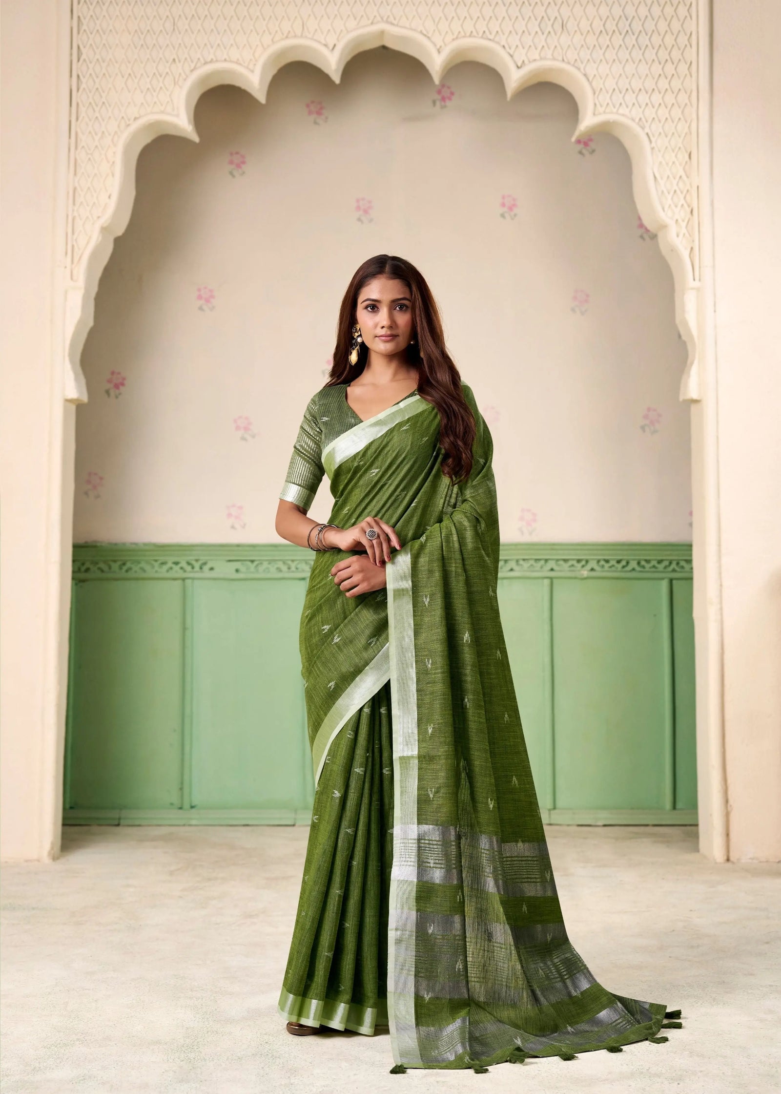 Woman wearing a green saree with a white border in front of an archway.