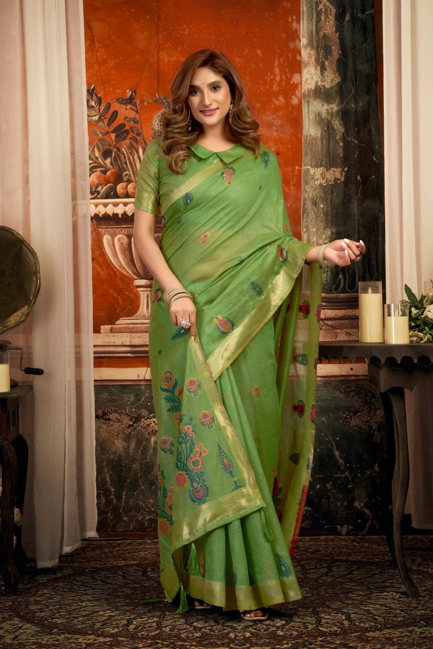 Woman in a green saree with floral patterns standing indoors.
