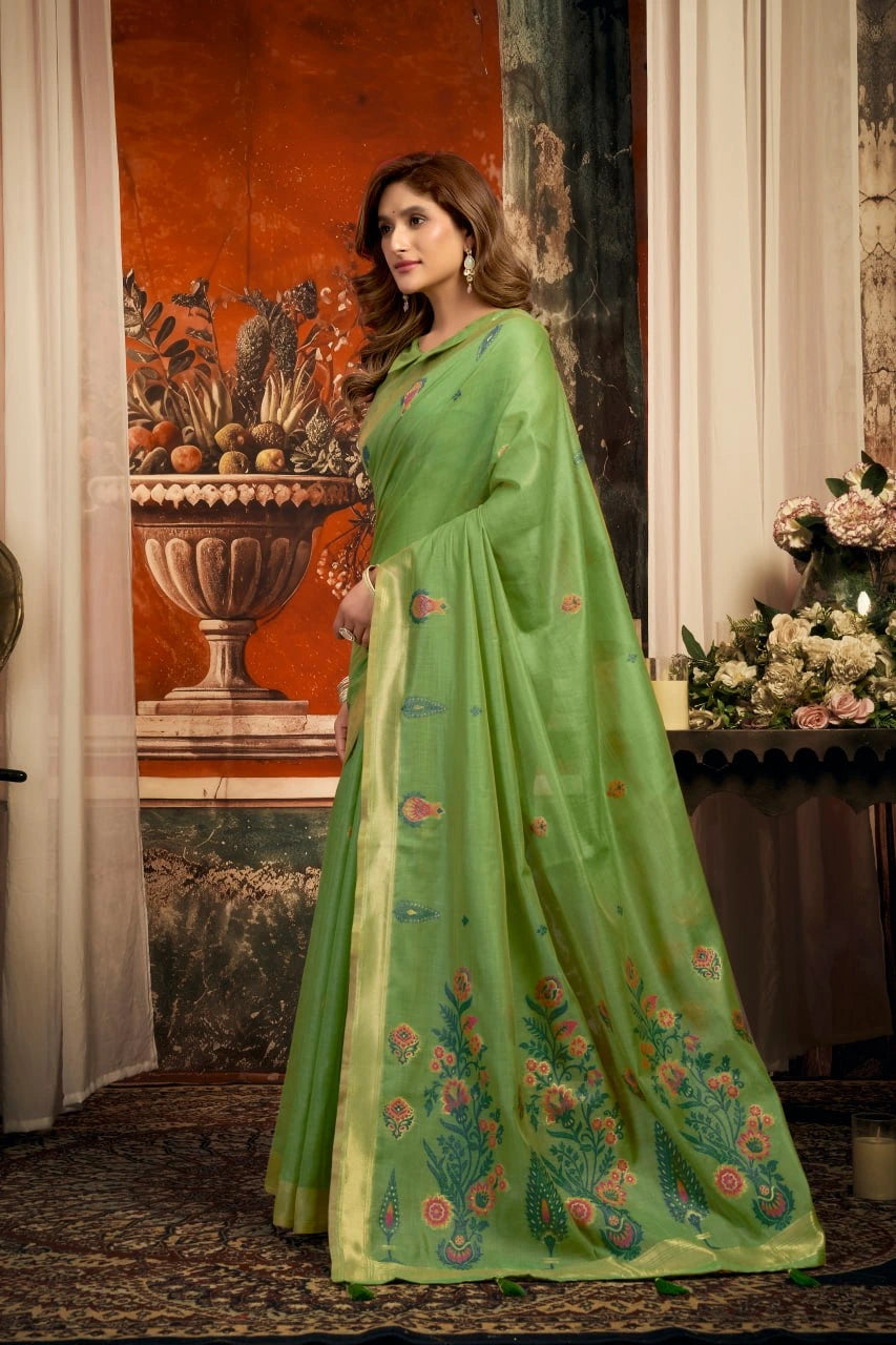 Woman in a green saree with floral patterns standing in an elegant interior setting.