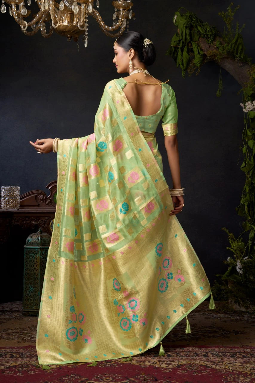 Woman in a green and yellow saree with floral patterns in a dark room.