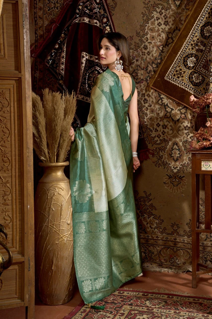 Woman in a green saree standing in an ornate room with decorative elements.