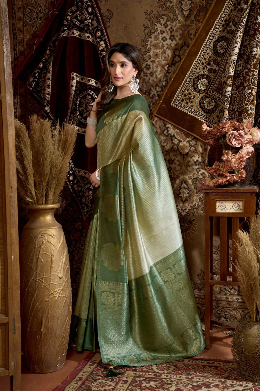 Woman in a green saree standing in an ornate room with decorative elements.