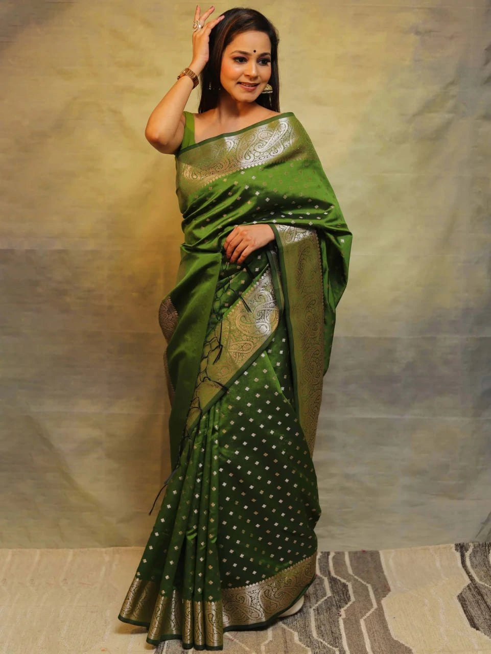 Woman wearing a green saree with gold patterns on a plain background