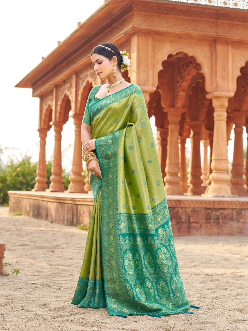 Woman in a green saree standing in front of an architectural structure.