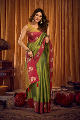 Woman in a green and red saree standing in front of a curtain.