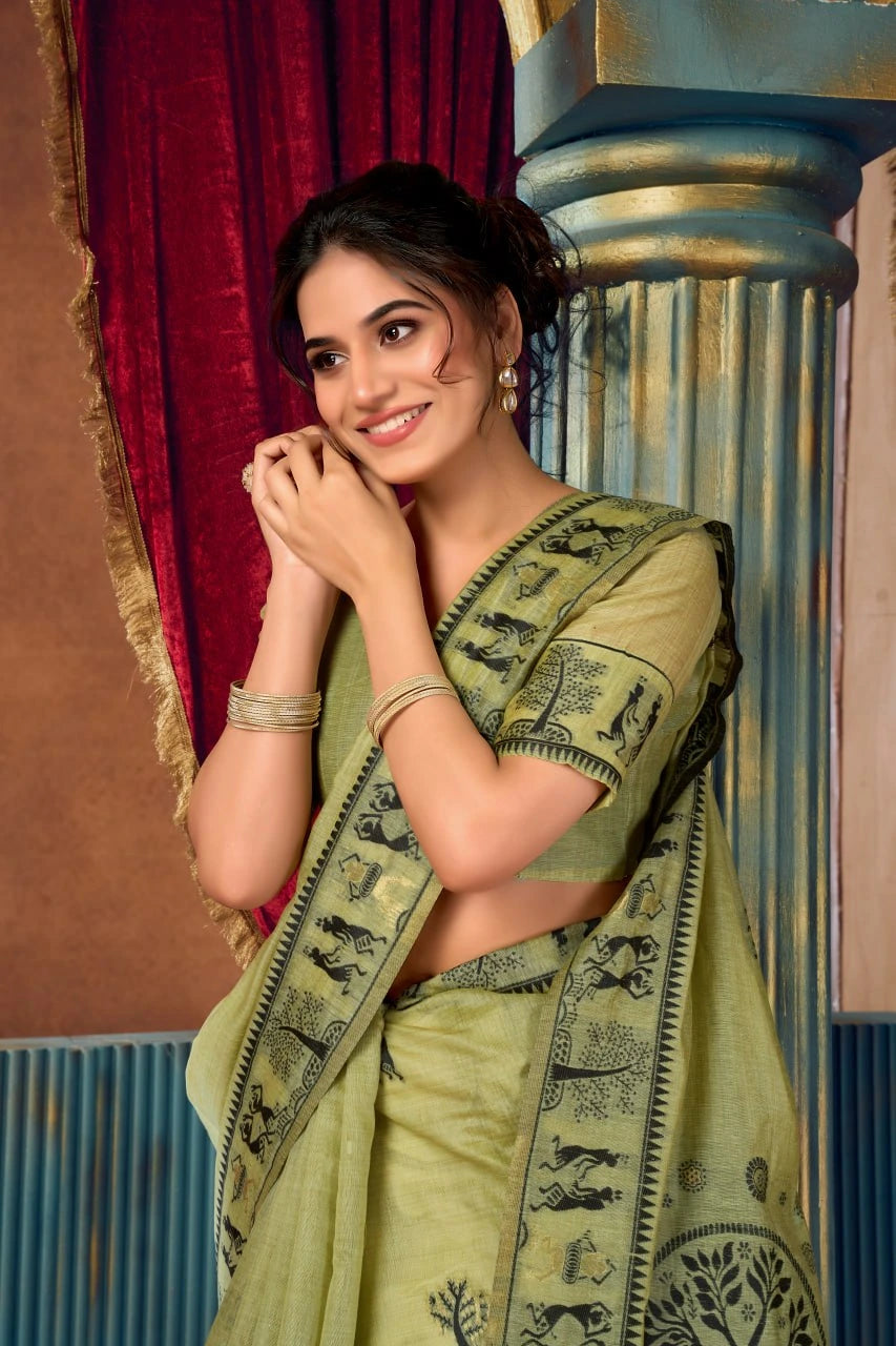 Woman in a green saree with elephant patterns standing against a decorative wall.