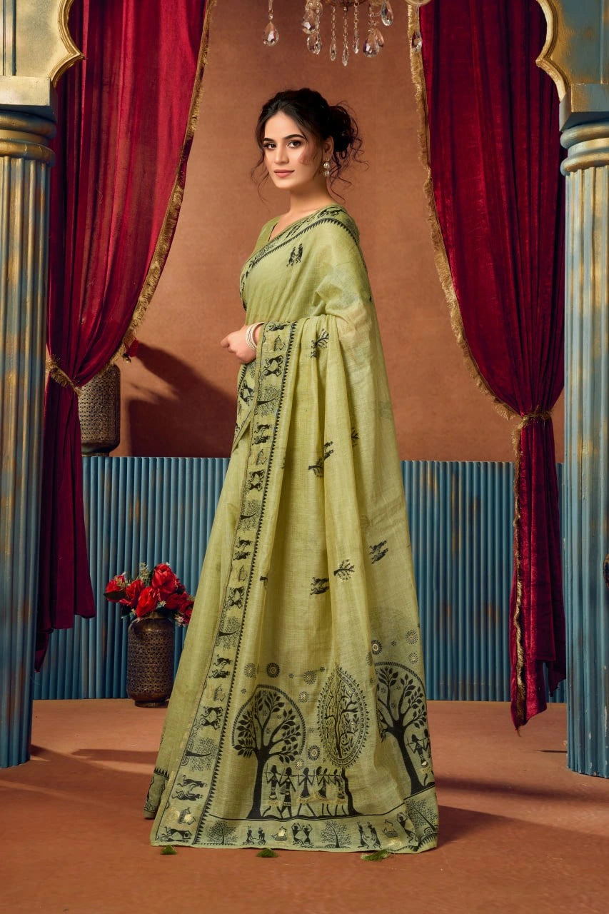 Woman in a green saree with black patterns standing in front of red curtains.