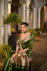 Woman in a green saree sitting outdoors with plants and columns in the background