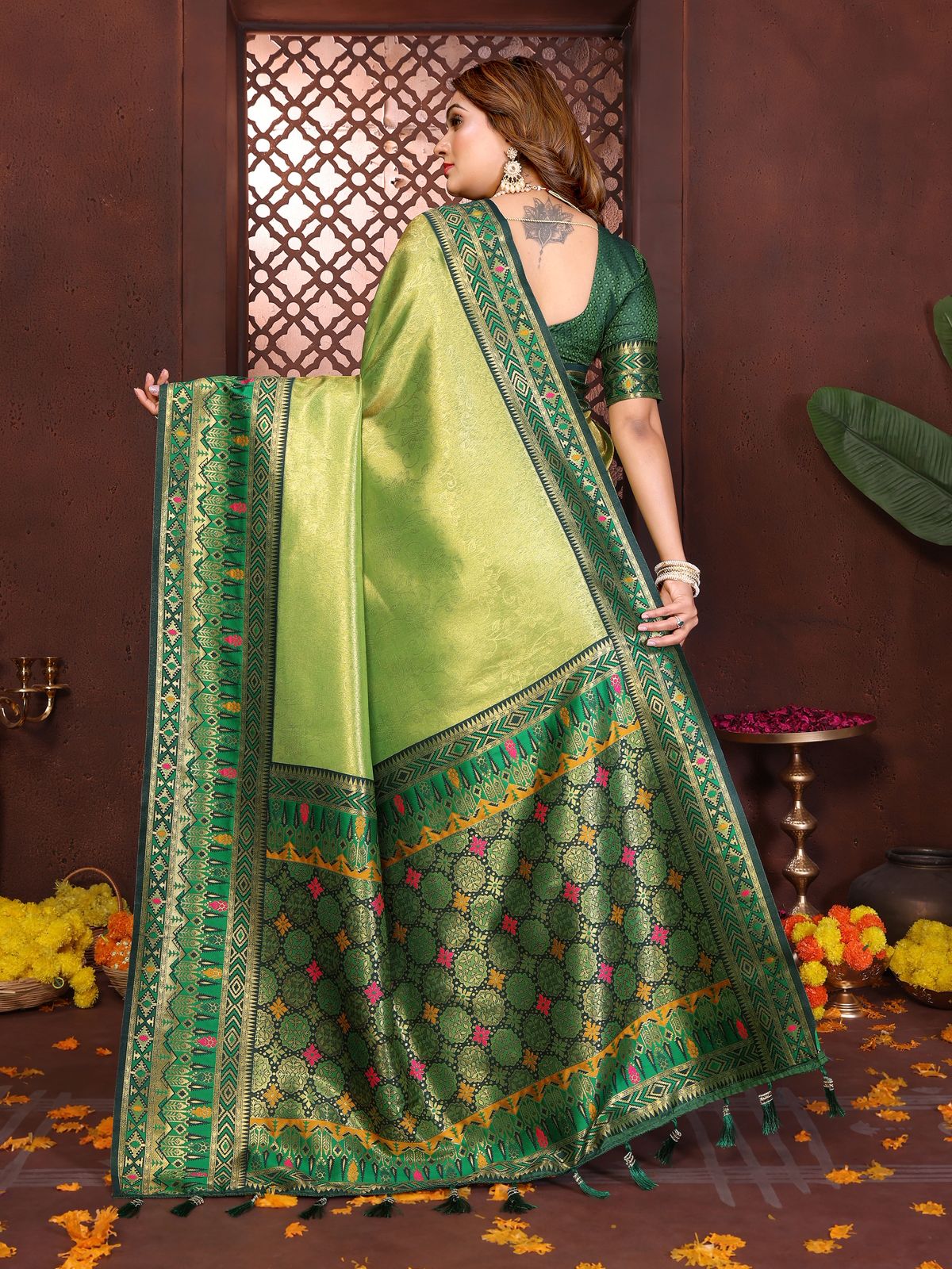 Woman wearing a green saree with a traditional design, standing against a decorative background.