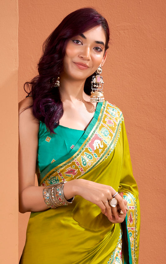 Woman wearing a green saree with gold border against a brown background