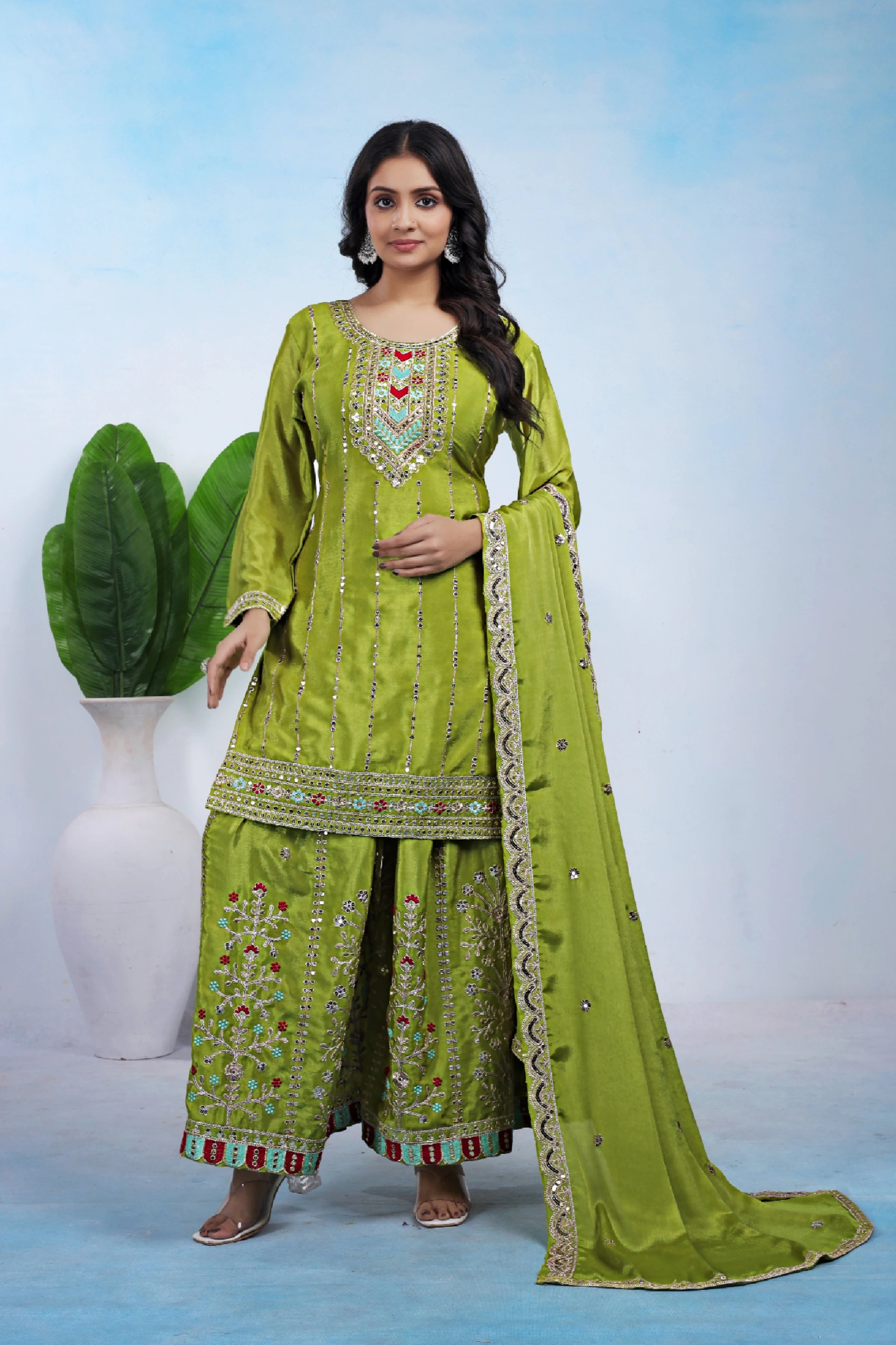 Woman wearing a green traditional outfit with a matching dupatta against a light blue background