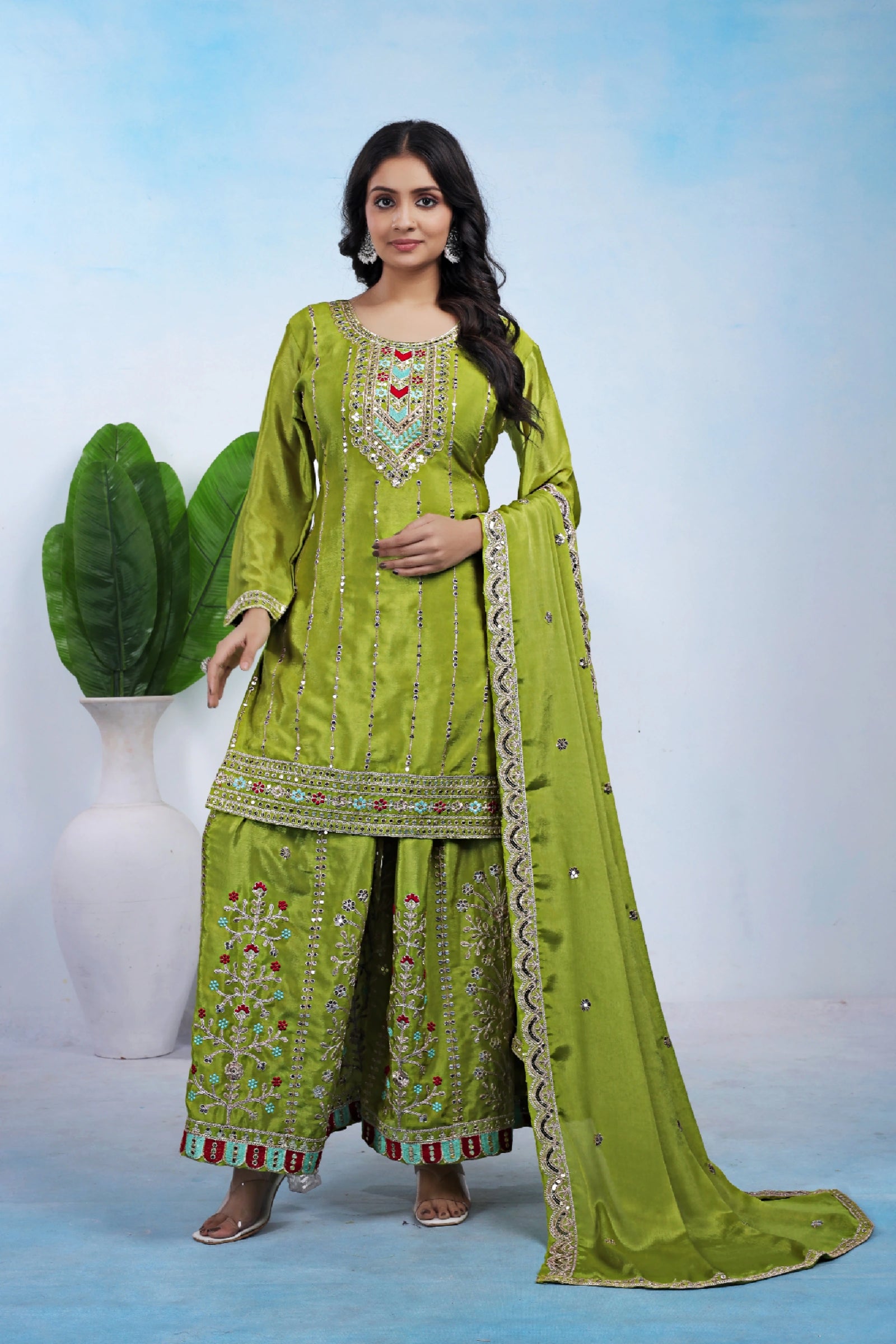 Woman wearing a green traditional outfit with a matching dupatta against a light blue background