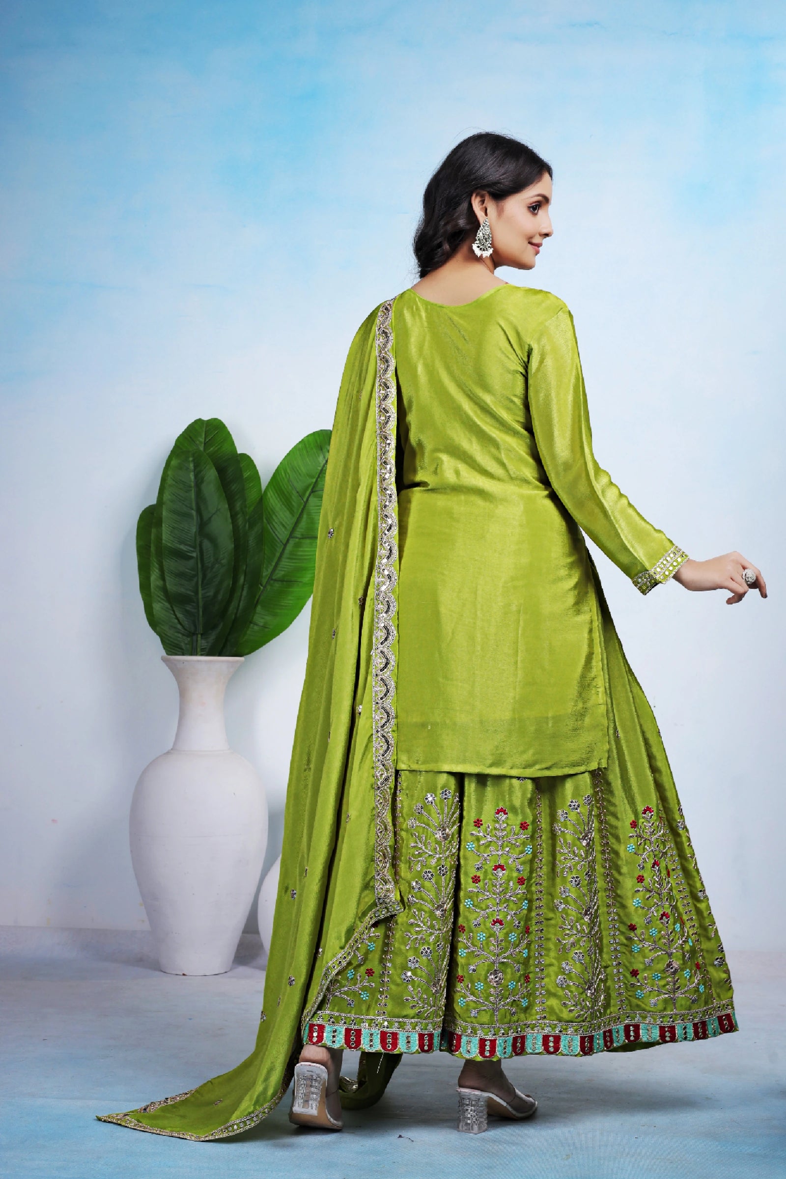 Woman in a green traditional outfit with a white vase and plant in the background