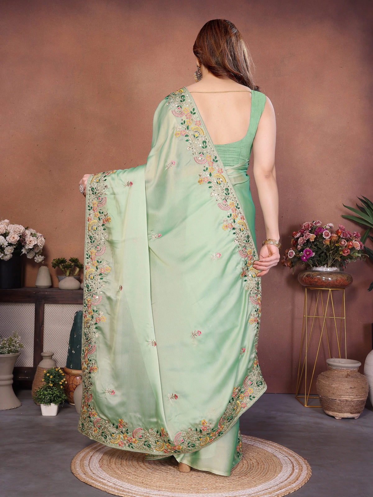 Woman wearing a light green saree with floral patterns in an indoor setting.