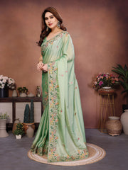 Woman wearing a light green saree with floral patterns in a decorated room.