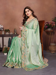 Woman wearing a light green saree with floral patterns in an indoor setting.