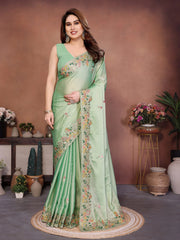 Woman wearing a light green saree with floral patterns in a decorated room.