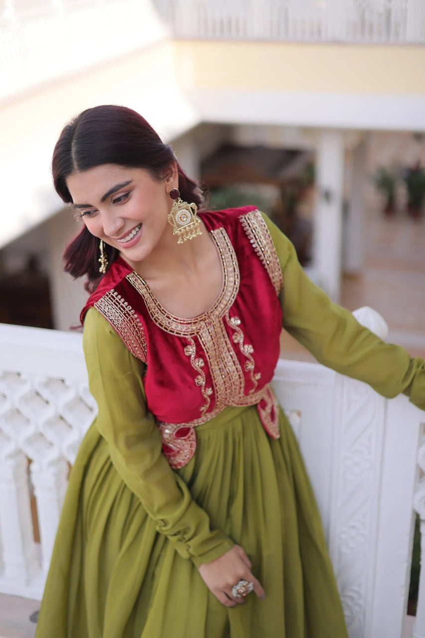 Woman in a red and green traditional outfit with gold embroidery, sitting on a white bench.