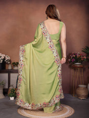 Woman wearing a light green saree with floral patterns in a room with decorative plants.