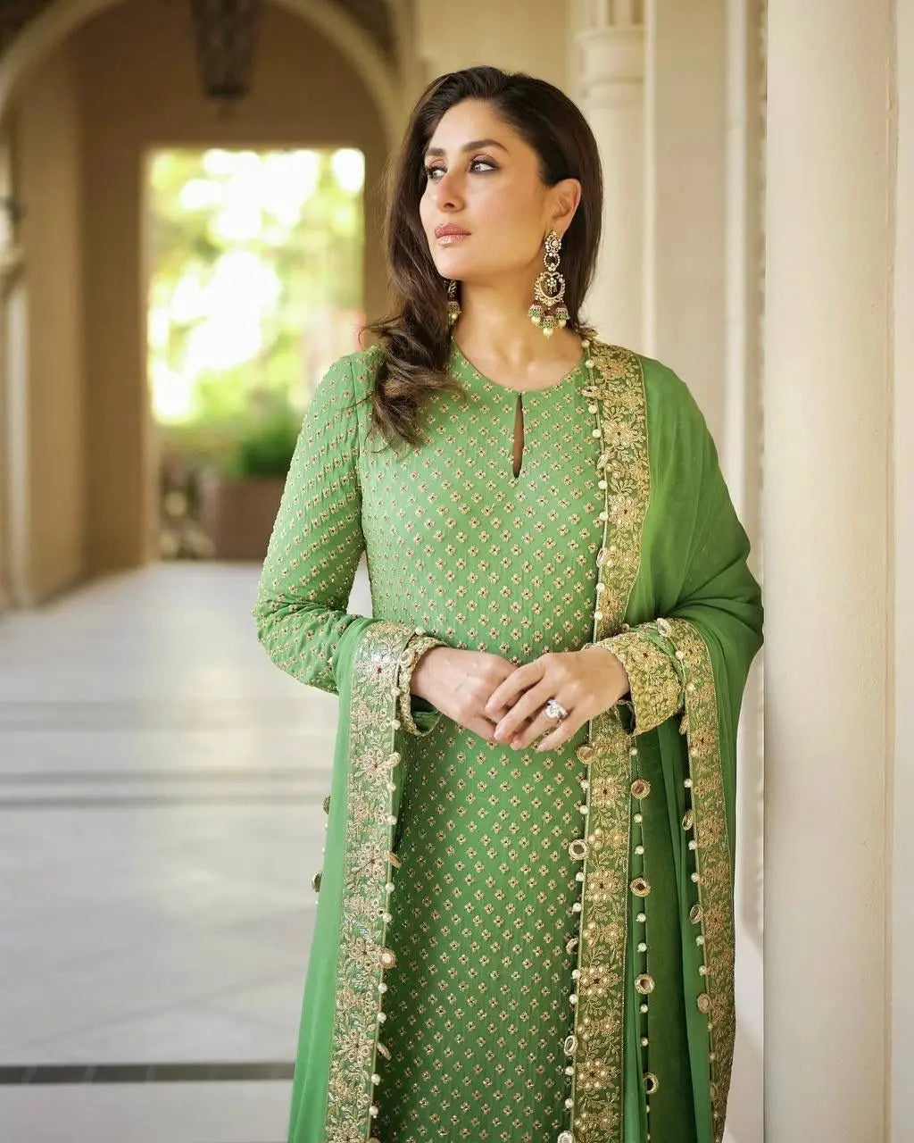 Woman in a green traditional outfit with gold embroidery standing in an outdoor setting.